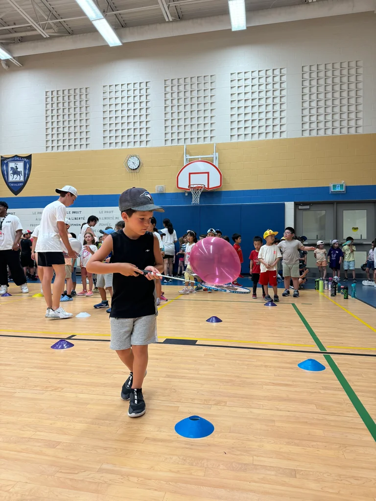 A camper confidently balances a balloon on a badminton racquet in a camp-wide-activity designed by teachers for fun, confidence building and team work
