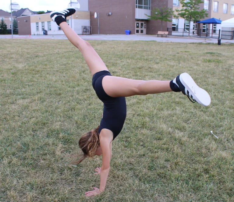 A child performs a cartwheel on a grassy field during an outdoor camp activity at Rouge Camps.