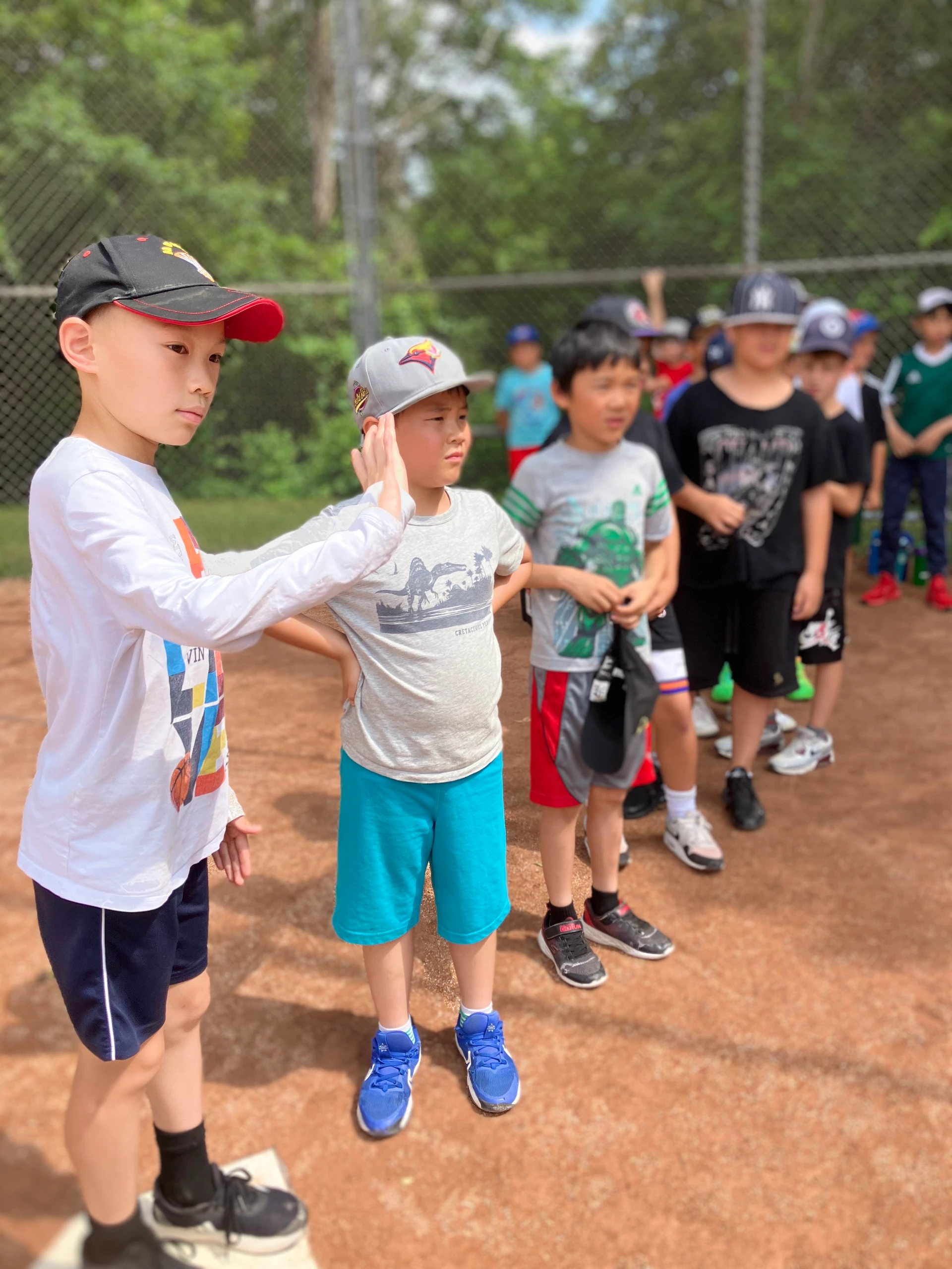 A group of campers connect in conversation while waiting for their turn to kick, during an outdoor game of soccer baseball at Rouge Camps Unionville.