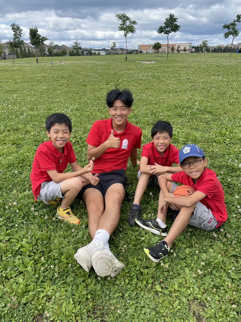 Three male campers hangout with a fully present camp staff at Rouge Camps Woodbridge on a sunny day.