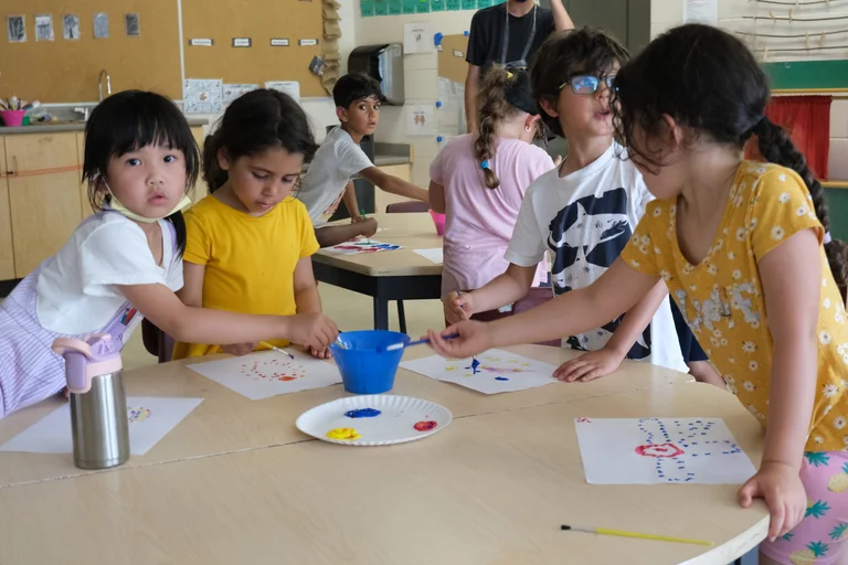 Children gather around a table painting on paper together during an indoor classroom activity at Rouge Camps Woodbridge.