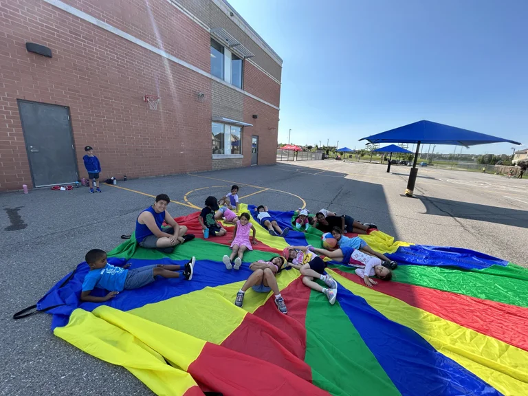 A group of Deer campers hanging out outside on a parachute at Rouge Camps Woodbridge.