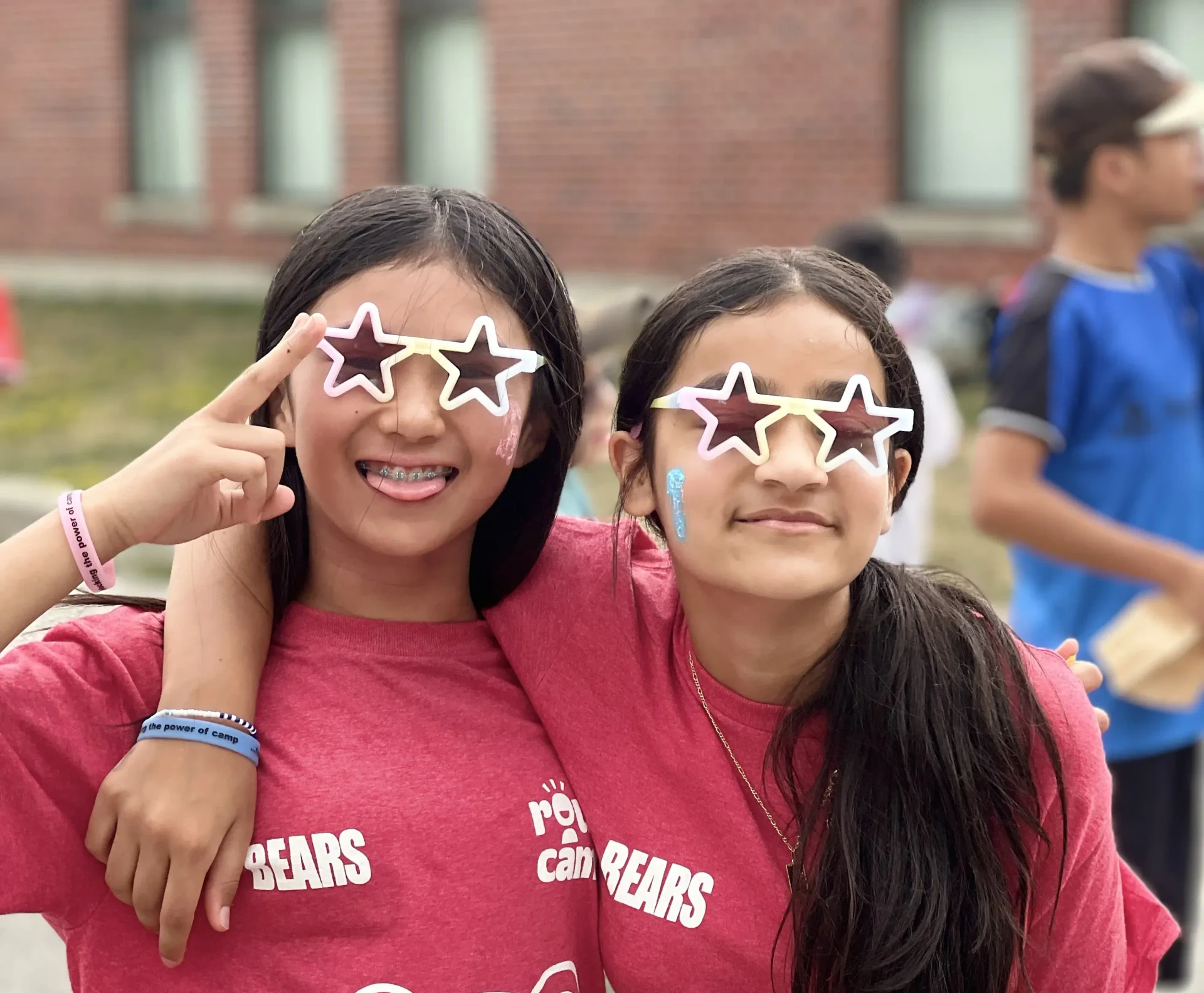 Two 11 year old girls pose wearing white star framed sunglasses in Rouge Camps t-shirts one with tongue out and the other with pursed lips full of attitude, completely silly and having fun at Rouge Camps Unionville.