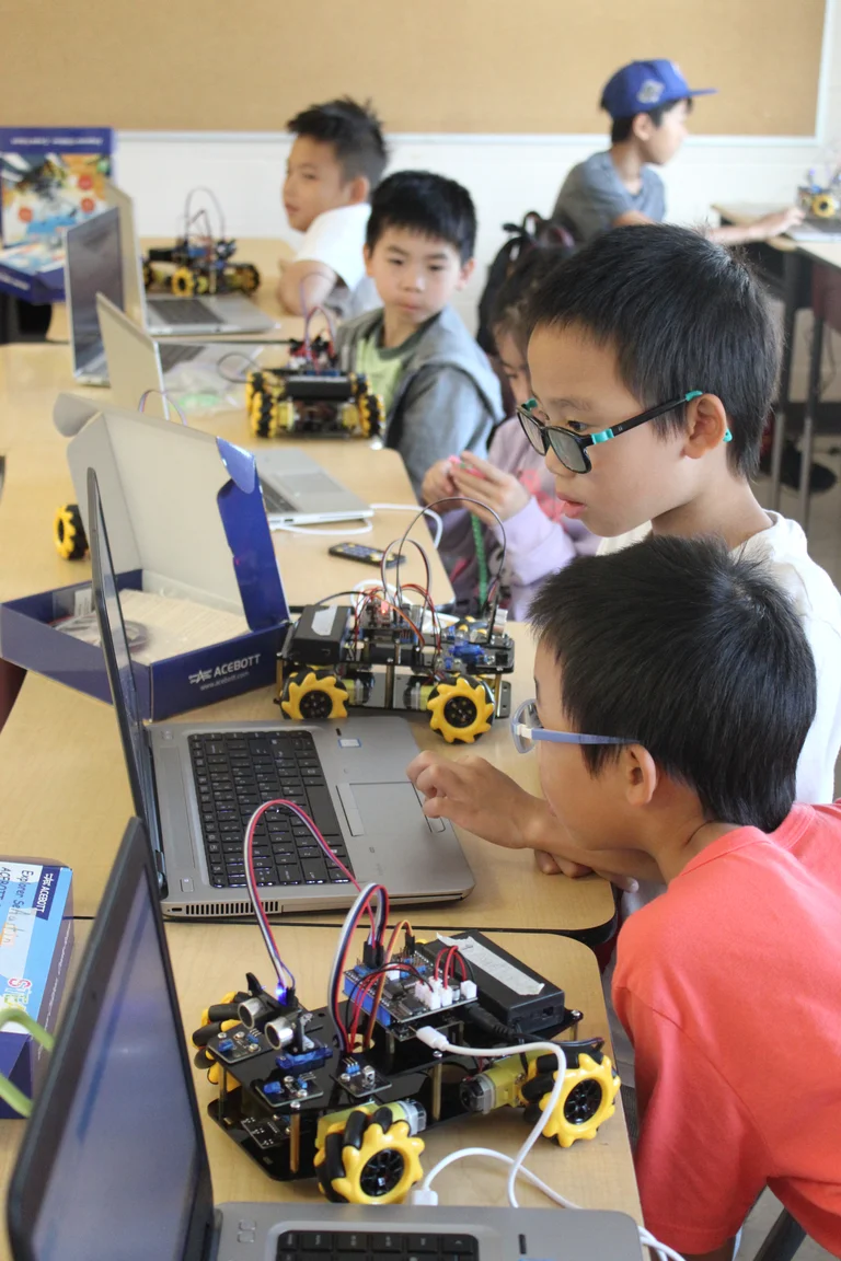 Children program small robots on laptops during a coding activity at Rouge Camps.