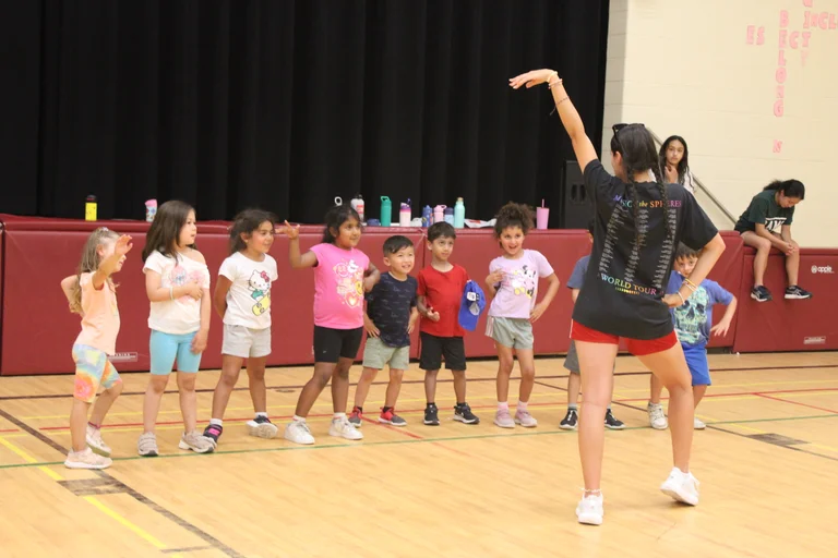 Children follow a counselor’s lead during a group dance activity in a gym at Rouge Camps Richmond Hill.