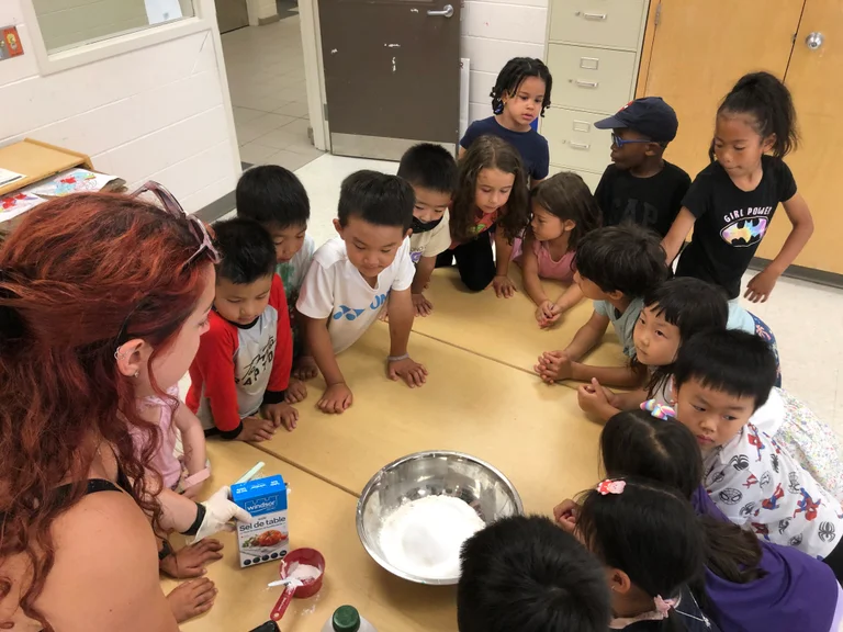 Children gather around a table watching a hands-on science activity with an instructor and materials at Rouge Camps Woodbridge.
