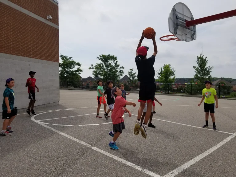 A Bear Camper elevates during a basketball elective for a jump shot on an outdoor basketball court at Rouge Camps Woodbridge.