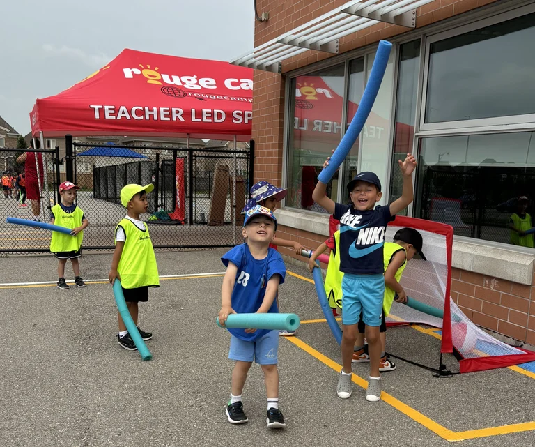 Campers celebrate with smiles and throwing their pool noodles up in the air after a goal in a game of pool noodle hockey at Rouge Camps Woodbridge.