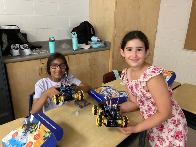Two female campers proudly show off their completed robots during ROUGE-botics at Rouge Camps.
