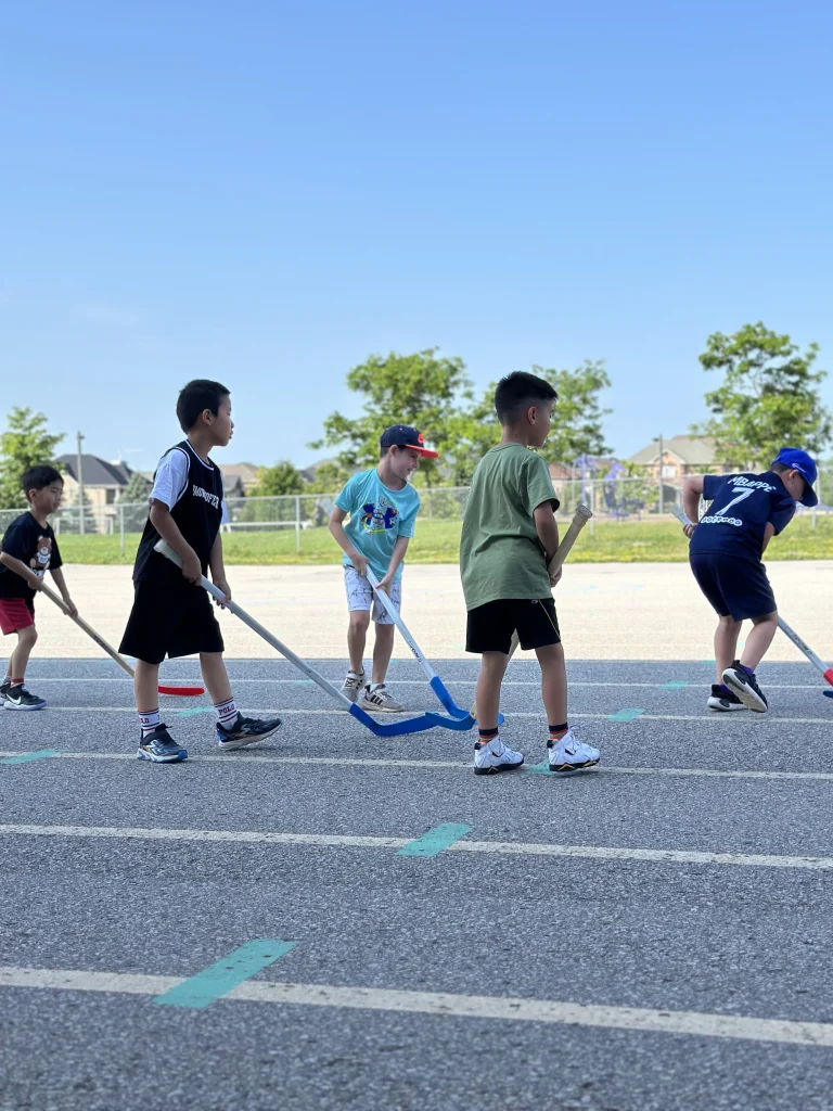 A group of Fox Campers play hockey outdoors on a sunny day at Rouge Camps.