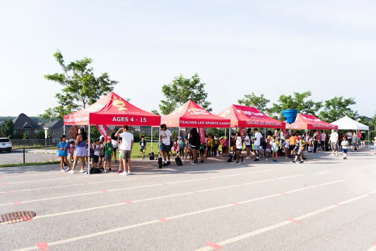 Wide shot of multiple red Rouge Camps tents set up outdoors during morning drop-off, with campers and staff gathered underneath on a sunny day at Rouge Camps Richmond Hill.