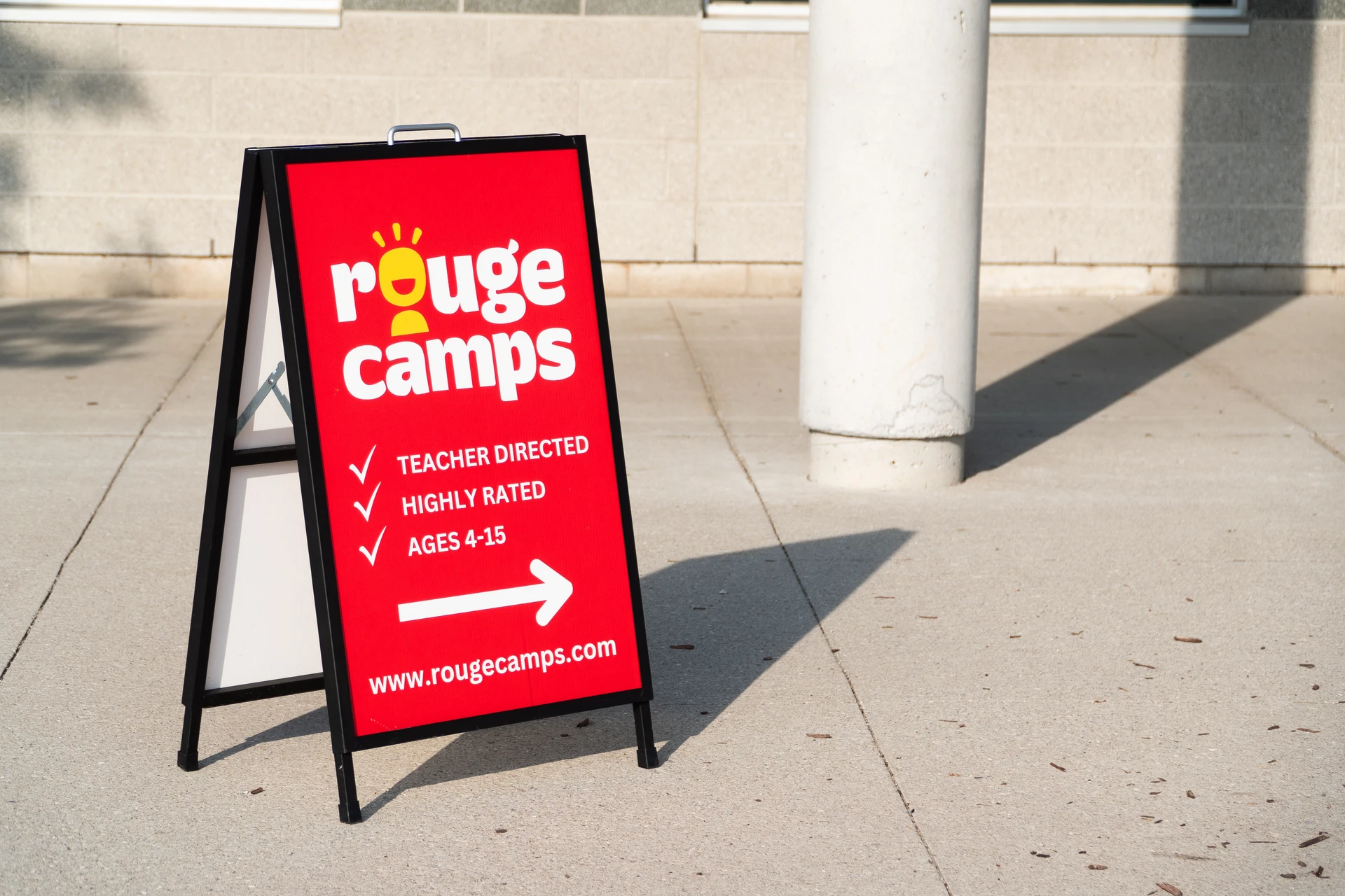 A bright Rouge Camps A-Frame sign directs parents to the drop-off area on the first day of camp.