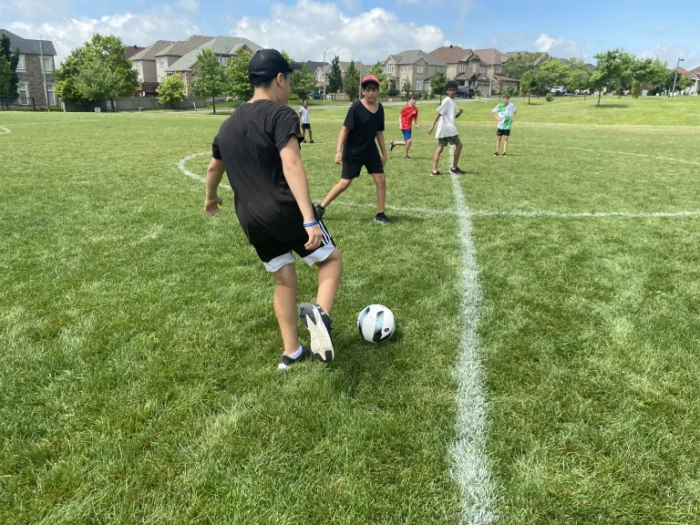 Campers play soccer at Rouge Camp on a green soccer field.