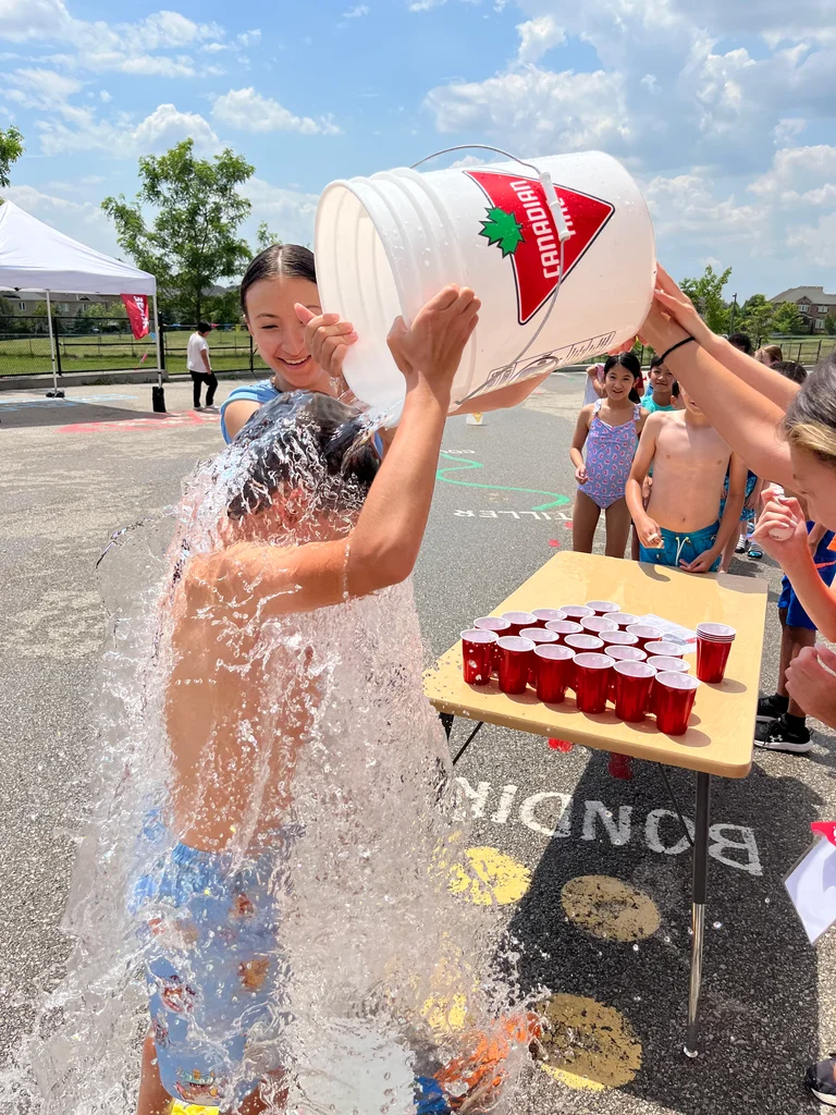 A camper willings gets a large bucket of water dumped on them as happy staff and campers look on during waterplay at Rouge Camps Richmond Hill.