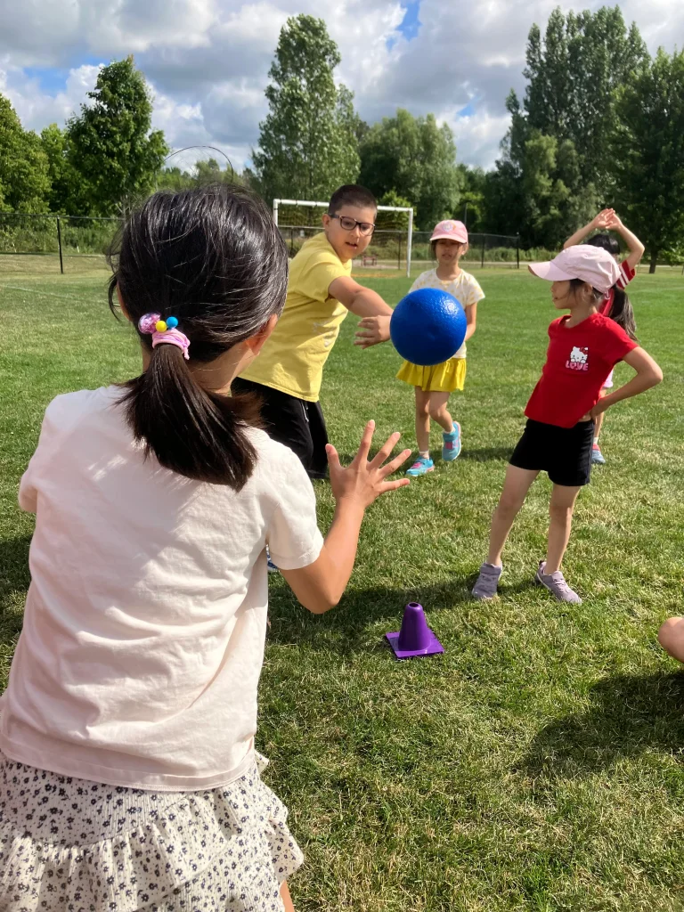 A camper throws a dodgeball as hard as they can outdoors on a field with friends at Rouge Camps.